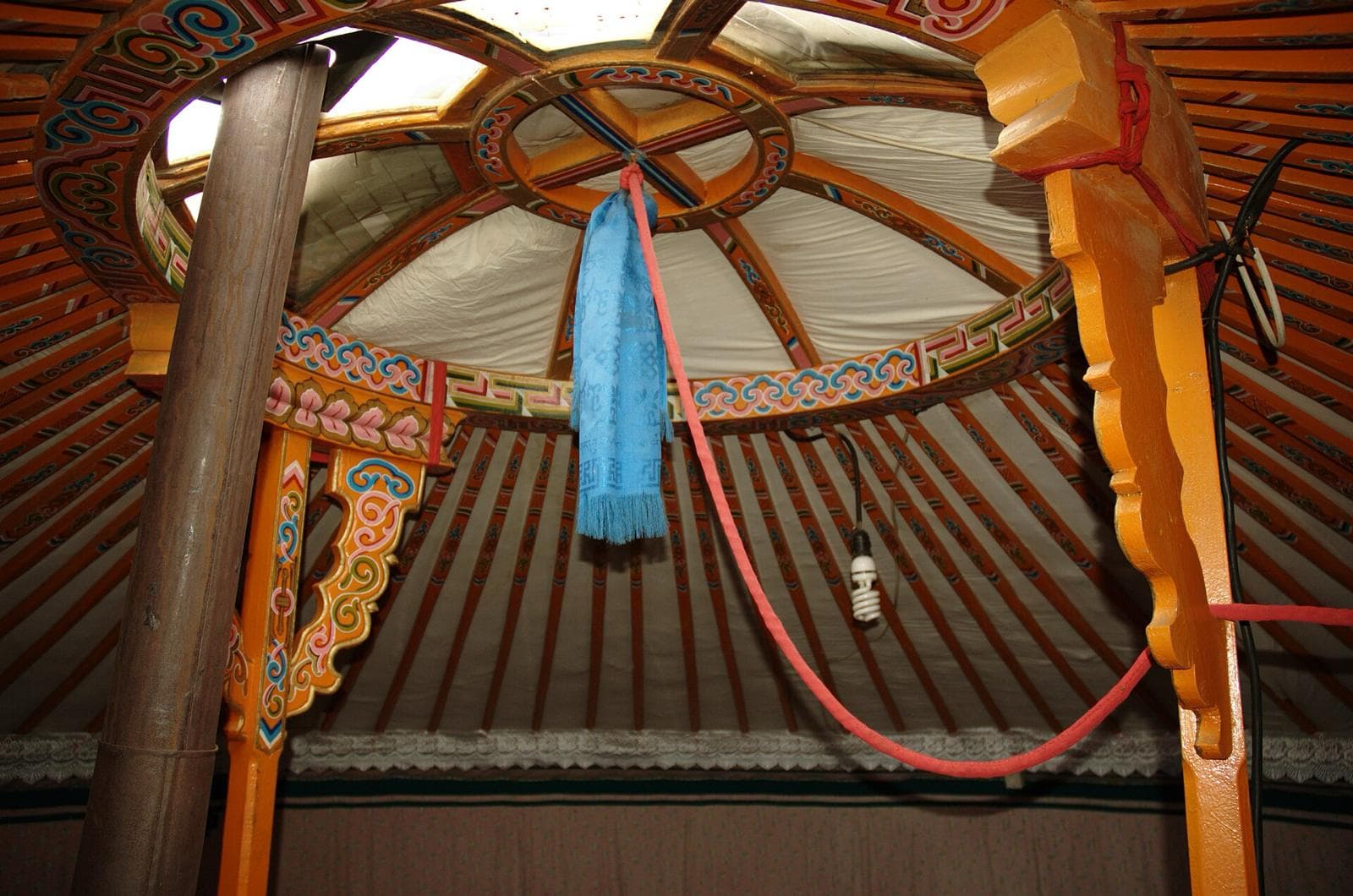 Inside a ger: the painted toono roof crown and posts, with a blue khadag hanging from the centre